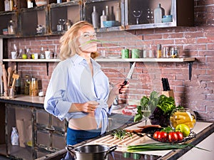 Blonde woman on kitchen playing with green onion