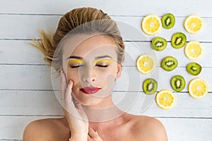 Blonde woman laying next to slices of lemon and kiwi