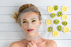 Blonde woman laying next to slices of lemon and kiwi