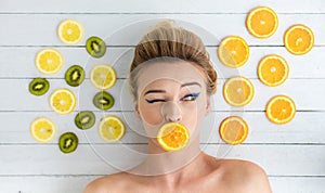 Blonde woman laying next to slices of orange, lemon and kiwi