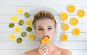 Blonde woman laying next to slices of orange, lemon and kiwi