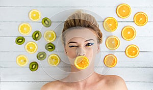 Blonde woman laying next to slices of orange, lemon and kiwi