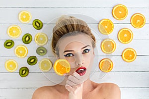 Blonde woman laying next to slices of orange, lemon and kiwi