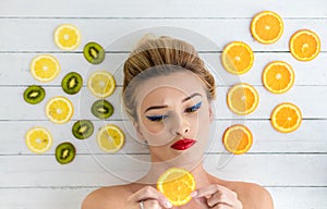 Blonde woman laying next to slices of orange, lemon and kiwi