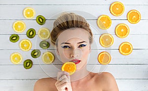 Blonde woman laying next to slices of orange, lemon and kiwi