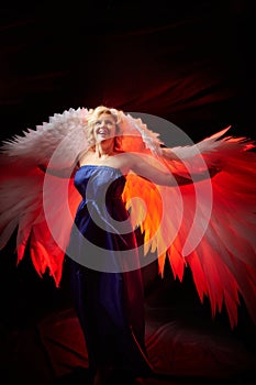 Blonde woman with a long blue dress and white angel wings. Photo shoot in studio