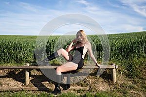 Blonde woman with long hair, young and beautiful dressed in black dress and black boots sitting sensually on wooden fence with one
