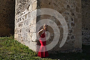 Blonde woman with long hair, young and beautiful, wearing a long red dress and a crown of flowers on her head, leaning against the