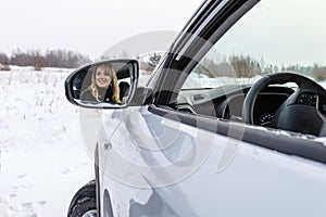 Blonde woman looking in the car rear-view mirror and smiling