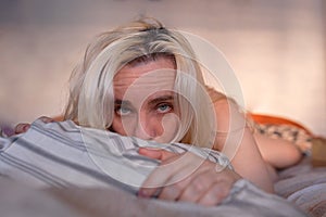 Blonde woman lying in bed with messy hair, depressed and lonely