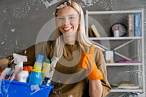 Blonde woman maid holding basket full of cleaning products