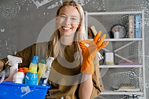 Blonde woman maid holding basket full of cleaning products