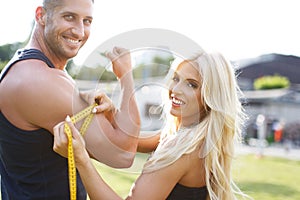 Blonde woman measure mans biceps by yellow measuring tape