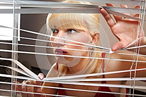 Blonde woman observes through blinds