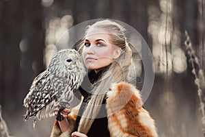 Blonde woman with an owl in her hands walks in the woods in autumn and spring. Long hair girl, romantic portrait with owl. Art fa