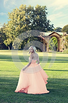 Blonde woman in peach color tulle ball dress walking in formal garden