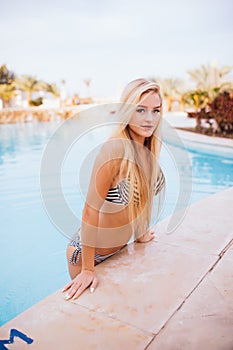 blonde Woman With Perfect Curvy Body Shape In Fashionable Bikini Swimwear Relaxing At Swimming Pool Edge.