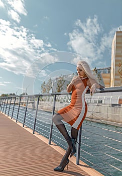 Blonde woman with perfect legs in pantyhose and shoes with high heels posing on the bridge