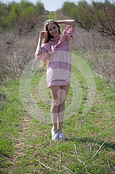 Beautiful blonde woman in pink dress on the road in the garden in the spring