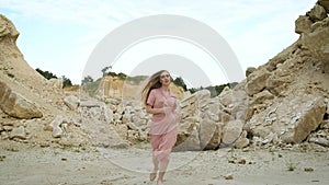 Blonde woman in a pink dress whitens and poses in front of the camera on a sand pit. Model