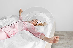 Blonde woman in pink pajamas, sleep mask wake up, stretches