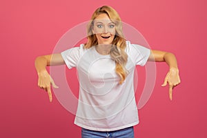 Blonde woman pointing fingers downward with excitement over pink background