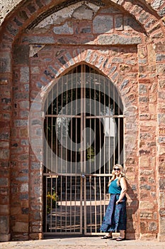 Blonde woman poses in front of a locked gate at an ancient tomb in New Delhi India