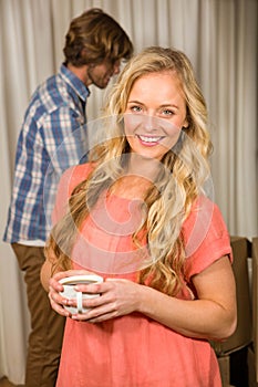 Blonde woman posing with a mug with her boyfriend behind