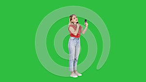 Blonde woman preening in front of the smartphone on a green screen, chroma key.