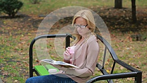 Blonde Woman Reading Book on Brench in Autumn Park.