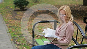 Blonde Woman Reading Book on Brench in Autumn Park.