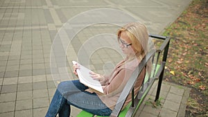 Blonde Woman Reading Book on Brench in Autumn Park.