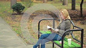 Blonde Woman Reading Book on Brench in Autumn Park. drinking hot coffee or tea