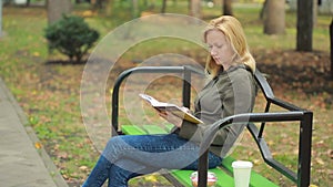 Blonde Woman Reading Book on Brench in Autumn Park. drinking hot coffee or tea