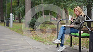 Blonde Woman Reading Book on Brench in Autumn Park. drinking hot coffee or tea