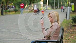 Blonde Woman Reading Book on Brench in Autumn Park. drinking hot coffee or tea