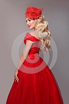 Blonde woman in red dress andBlonde woman in red dress and elegant hat isolated on studio grey background. Beautiful blond girk w