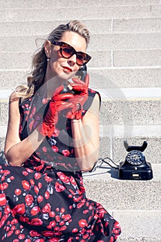 Blonde woman in red dress sitting on stair steps with vintage black telephone