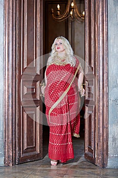 Blonde woman in red dress stands in doorway, photo