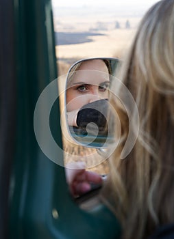 Blonde woman reflected in safari vehicle side mirror with the sunny landscape in the background