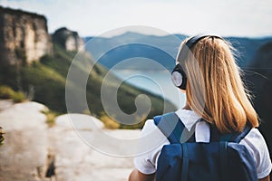 Blonde woman relaxing listening to music with headphones enjoying scenic view of nature on top of mountain, traveler