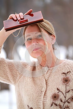 Blonde woman in retro tan sweater with vintage bag looking into the distance outside in winter hat with feathers Stevie Nicks vibe