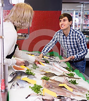 Blonde woman selling fish to male customer in store