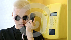 blonde woman with short haircut picks up phone in yellow telephone booth and talks on phone. concept of special agent
