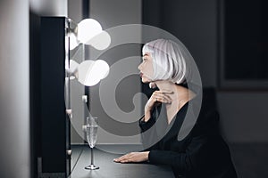 Blonde woman sitting and looking at mirror in dressing room