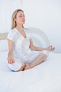 Blonde woman sitting in lotus pose in bed