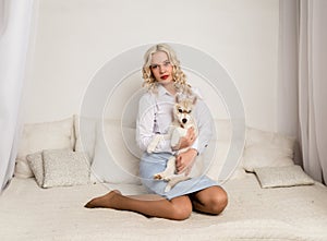 Blonde woman sitting on a sofa with puppy husky dog. girl playing with a dog