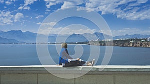 Blonde woman sitting on the wall and watching sea