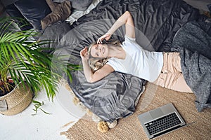 Blonde woman speaking phone working, making video call, watching movie on a laptop in cozy home bedroom modern interior.