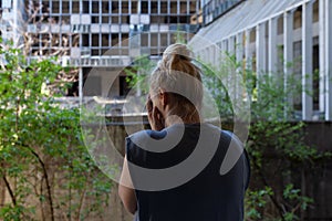 Blonde woman standing in front abandoned destroyed building, covering face with hands